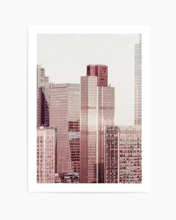 Photography art print featuring a cityscape of modern skyscrapers in muted rose and warm grey tones against a bright white sky. The composition captures sunlight reflecting off the windows of the central buildings, creating a subtle lens flare effect.
