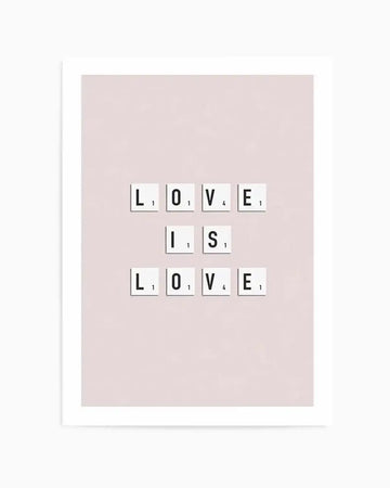 Art print featuring the phrase "LOVE IS LOVE" spelled out in white Scrabble-style letter tiles with black letters and point values, arranged in three rows on a soft blush pink background, with a white frame and white border.