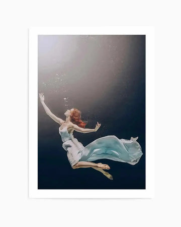 "Photography art print featuring a woman with red hair floating underwater in a white dress, reaching upwards towards the light. The composition shows her body gracefully suspended in dark blue water with light rays and small bubbles visible from above."
