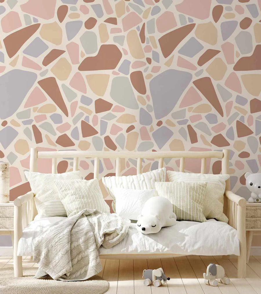 Nursery:
Peel and stick wallpaper featuring a repeating pattern of abstract, irregular shapes in muted tones of dusty rose, pale blue, soft grey, warm beige, and light brown against a cream background, displayed above a white wooden daybed in a child's room. The daybed is adorned with white and cream pillows, a textured cream throw, and a white polar bear plush toy. Two small elephant toys sit on the light wood floor.