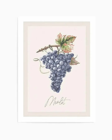 Watercolour art print featuring a bunch of deep purple grapes on a vine with green and reddish-brown leaves, set against a pale pink background. The word "Merlot" is written in elegant script below the grapes. The print is displayed in a white frame with a cream border.