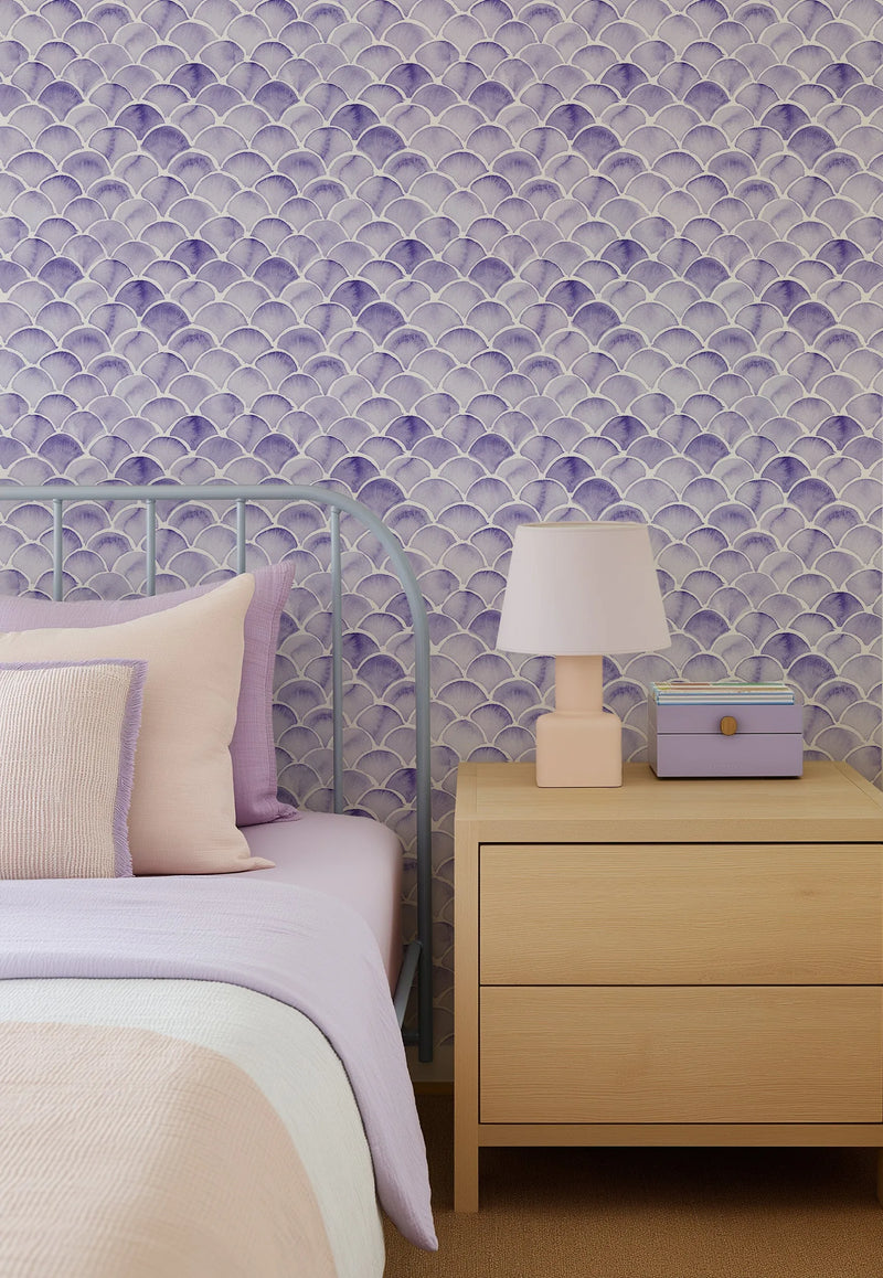 "Peel and stick wallpaper featuring a repeating pattern of hand-painted mermaid scales in varying shades of lavender and deep purple on a soft white background. The scalloped design has a loose, organic watercolour quality with visible brushstroke texture."
