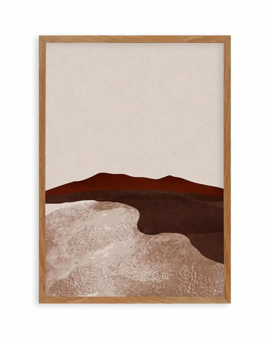 Abstract art print featuring a minimalist desert landscape with a deep reddish-brown mountain range against a pale cream sky. Below the mountains, a dark brown undulating shape meets a textured, lighter brown and cream foreground, suggestive of sand dunes or a dry riverbed. The print is displayed in a natural oak frame with a white border.