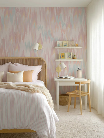 "A child's bedroom featuring a wall covered in Molten Wave wallpaper, showcasing a repeating pattern of vertical, abstract brushstrokes in soft pastel shades of pink, blue, yellow, and cream, creating a gentle, flowing design. The wallpaper serves as a backdrop for a light wood rattan headboard, a bed dressed in white and pink striped bedding with a cream textured throw, and a white desk with a natural wood chair. The room is softly lit by natural light from a window with sheer white curtains."