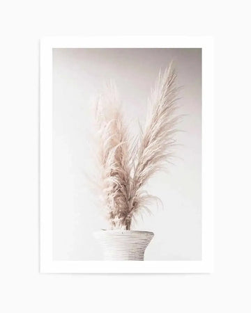 Art print titled "Navire de la Pampa" featuring dried pampas grass in muted beige and cream tones arranged in a white ribbed ceramic vase against a soft, neutral background. The composition has a minimalist, botanical aesthetic with delicate feathery plumes rendered in a soft, watercolor-like style. The artwork is mounted on white paper with a thin white border and displayed in a white frame.