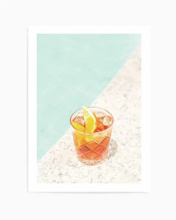 Art print featuring a vibrant orange cocktail in a textured glass, garnished with an orange slice and ice, set on a speckled white surface next to a light blue background, creating a diagonal split composition.