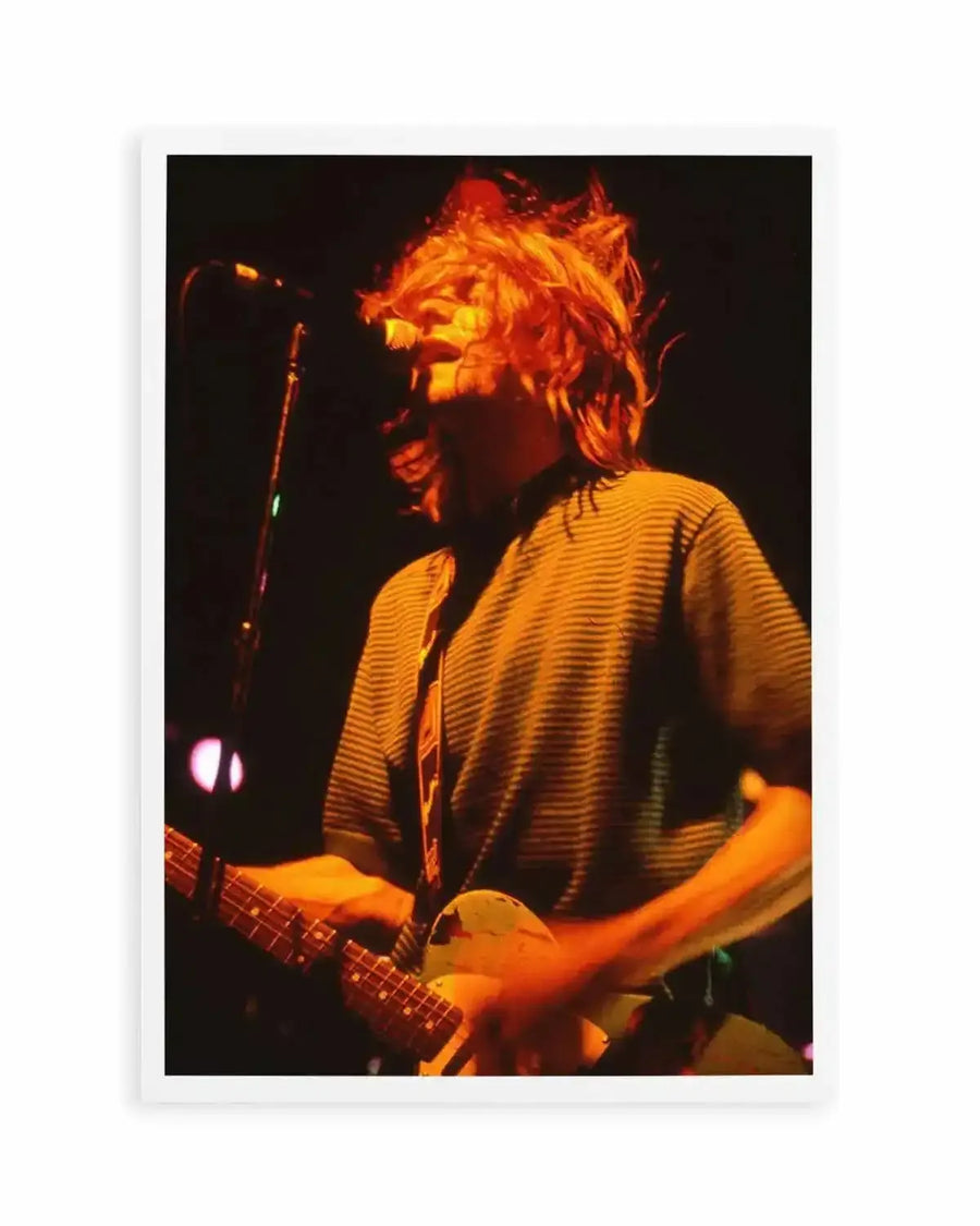 "Art print featuring a close-up, warm-toned photograph of a musician with long, messy, light brown hair playing an electric guitar and singing into a microphone on a dark stage. The musician is wearing a horizontally striped t-shirt and a guitar strap, with their face illuminated by an orange stage light, creating a dynamic and energetic composition."