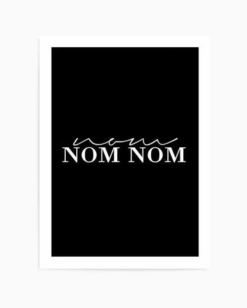 Art print on black background featuring the text "NOM NOM NOM" in white serif capital letters with a delicate cursive line flourish above it. The print is mounted on white paper with a white border, creating a minimalist, typographic design with high contrast between the black and white elements.