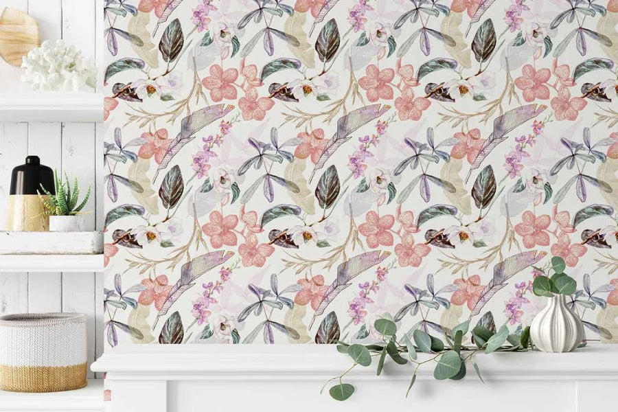 Oriental Orchids Wallpaper displayed on a wall showing a repeating botanical pattern featuring dusty rose and mauve orchid flowers, purple and green feathered leaves, and brown seed pods illustrated in a watercolor style against a cream background. The wallpaper is shown in a bright room setting with white shiplap walls, a white shelf displaying a potted succulent, woven storage baskets, and a white vase with eucalyptus branches in the foreground.