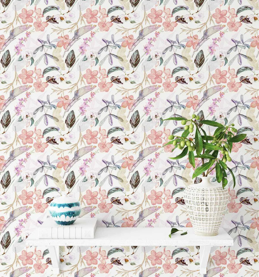Oriental Orchids Wallpaper displayed on a wall behind a white floating shelf. The wallpaper features a repeating pattern of delicate watercolor botanical illustrations including pink and coral orchid flowers, purple and gray feathered leaves, small brown insects, and tan botanical elements on a cream background. A white woven basket holding fresh green foliage sits on the shelf alongside a small blue and white decorative bowl.