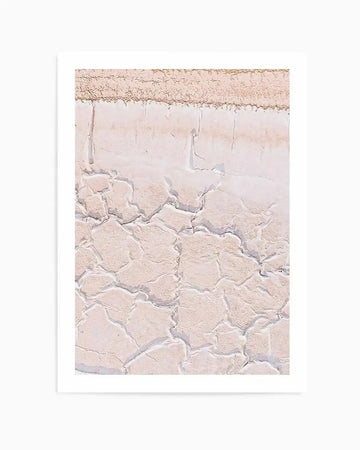 "Photography art print featuring a close-up of cracked, dry earth in shades of pale pink and cream, with a textured, rough surface. The composition captures the intricate patterns and lines of the parched ground, suggesting a desert or salt flat landscape."