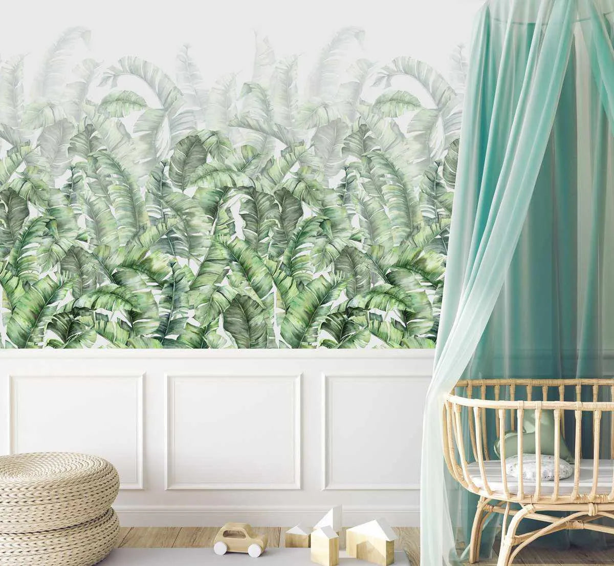 Nursery:
"Peel and stick wallpaper featuring a repeating pattern of hand-painted banana leaves in varying shades of green, from deep emerald to soft sage, on a white background. The botanical design has a loose, organic watercolour quality with visible brushstroke texture. The wallpaper is displayed above white wainscoting in a nursery with a light wood floor, a rattan bassinet with a sheer mint green canopy, and woven poufs."