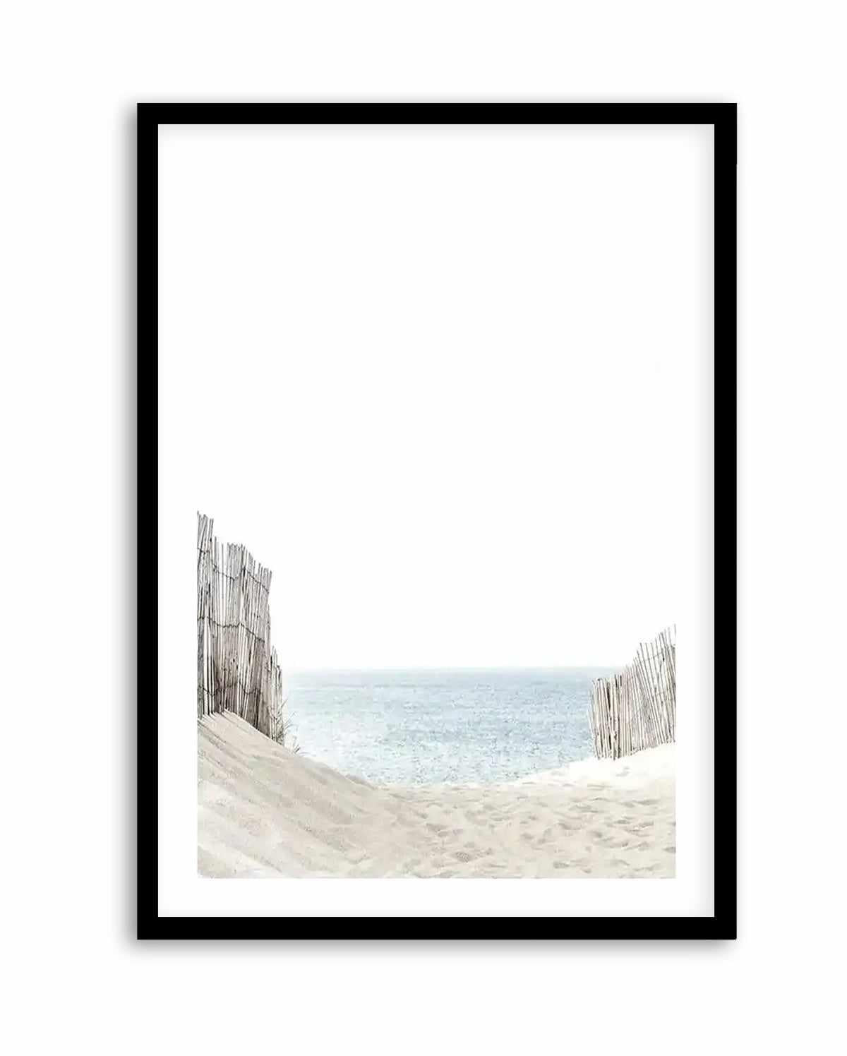 Framed art print titled "Path to the Sea" featuring a coastal landscape photograph. The image shows weathered wooden dune fences flanking sandy beach in soft beige and tan tones, with calm turquoise-blue ocean and pale sky beyond. The photograph has a serene, minimalist composition with the fences creating a natural frame. Displayed in a black frame with white border.