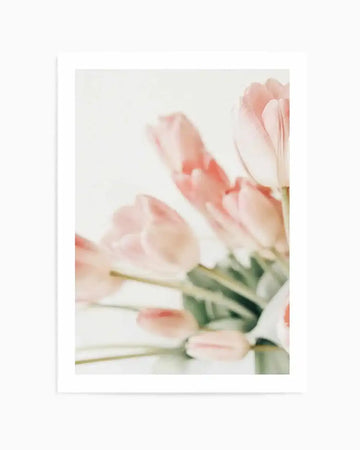 Soft focus photograph of a bouquet of pale pink tulips with long green stems on a light background. The composition features several tulip blooms in various stages of opening, with a dreamy, ethereal quality.