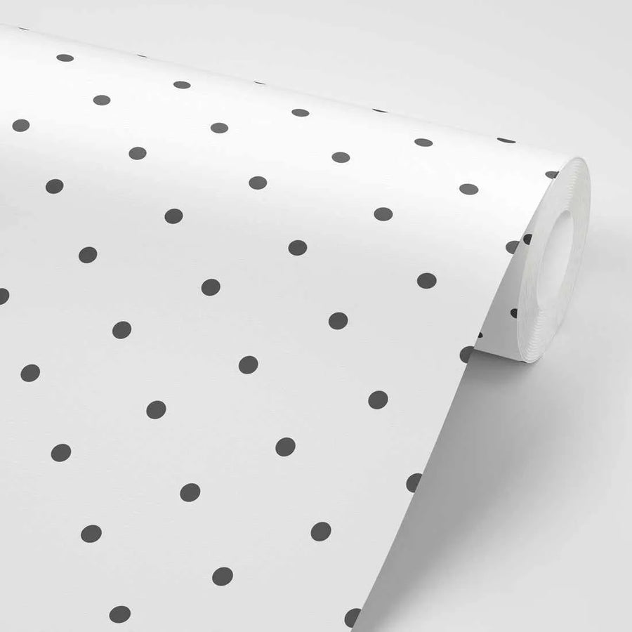 Peel and stick wallpaper featuring a repeating pattern of evenly spaced dark grey polka dots on a clean white background. The wallpaper is shown partially unrolled, creating a gentle curve and highlighting the matte finish of the paper.