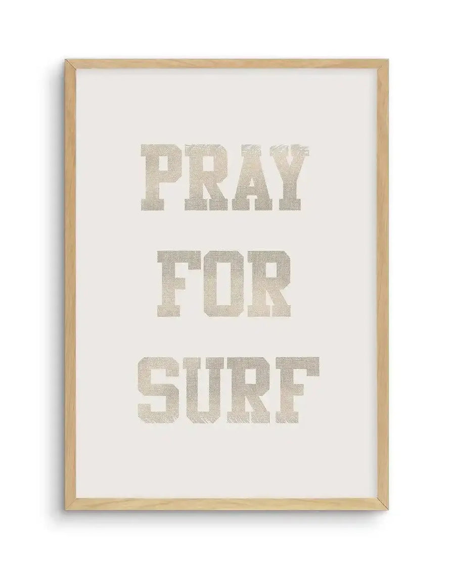 Art print featuring the words "PRAY FOR SURF" in three lines, rendered in a distressed, collegiate-style font with a textured, light beige or off-white appearance against a slightly darker, warm cream background, displayed in a natural wood frame with a white border.