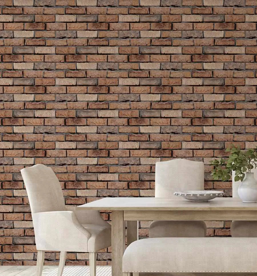 Dining Room:
"Red brick wallpaper displayed on a wall behind a light wood dining table and upholstered cream chairs in a modern dining room. The wallpaper features a repeating pattern of rectangular bricks in various shades of reddish-brown, terracotta, and muted grey, with visible texture and dark grey grout lines. A white ceramic vase with green foliage and a decorative bowl are on the table."