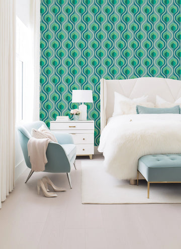 Bedroom featuring a wall covered in Retro Fun Wallpaper, displaying a repeating pattern of wavy, interlocking teardrop shapes in shades of teal, emerald green, and light grey. The wallpaper creates a vibrant, retro-inspired backdrop for a white upholstered bed with a tall headboard, a white nightstand with gold hardware, and a light blue armchair with a cream throw and pillow. A white faux fur blanket covers the bed, and a light blue tufted bench sits at the foot of the bed.