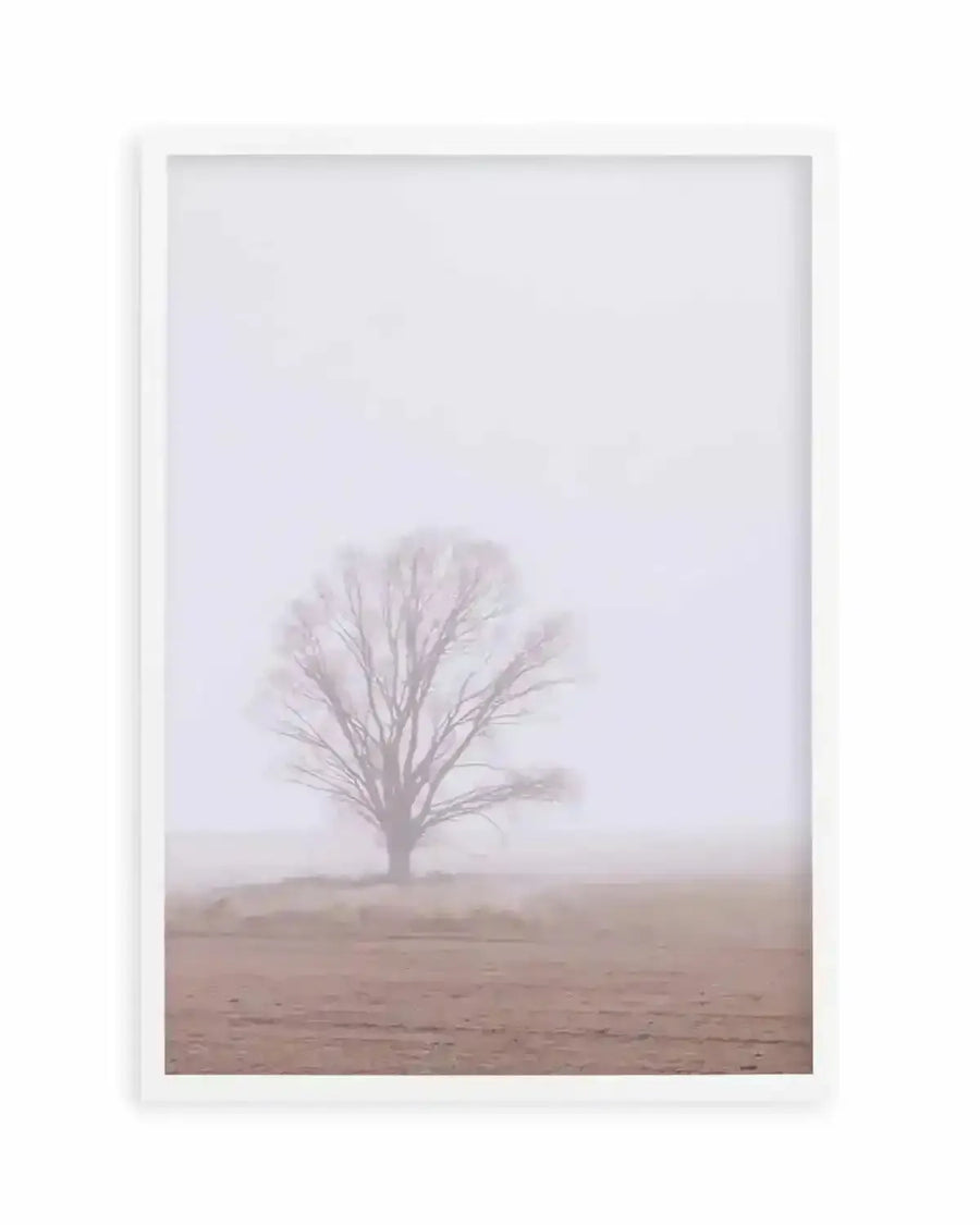 Framed photography art print of a solitary tree in a misty field, with a white frame and white border. The composition features a bare-branched tree silhouetted against a pale, hazy sky, with the foreground showing a muted brown field disappearing into the fog.