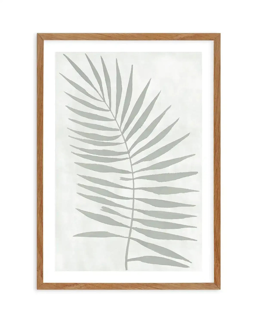 Watercolour art print featuring a single palm frond in a muted sage green against a soft white background with subtle brushstroke texture, displayed in a natural oak frame with white border.