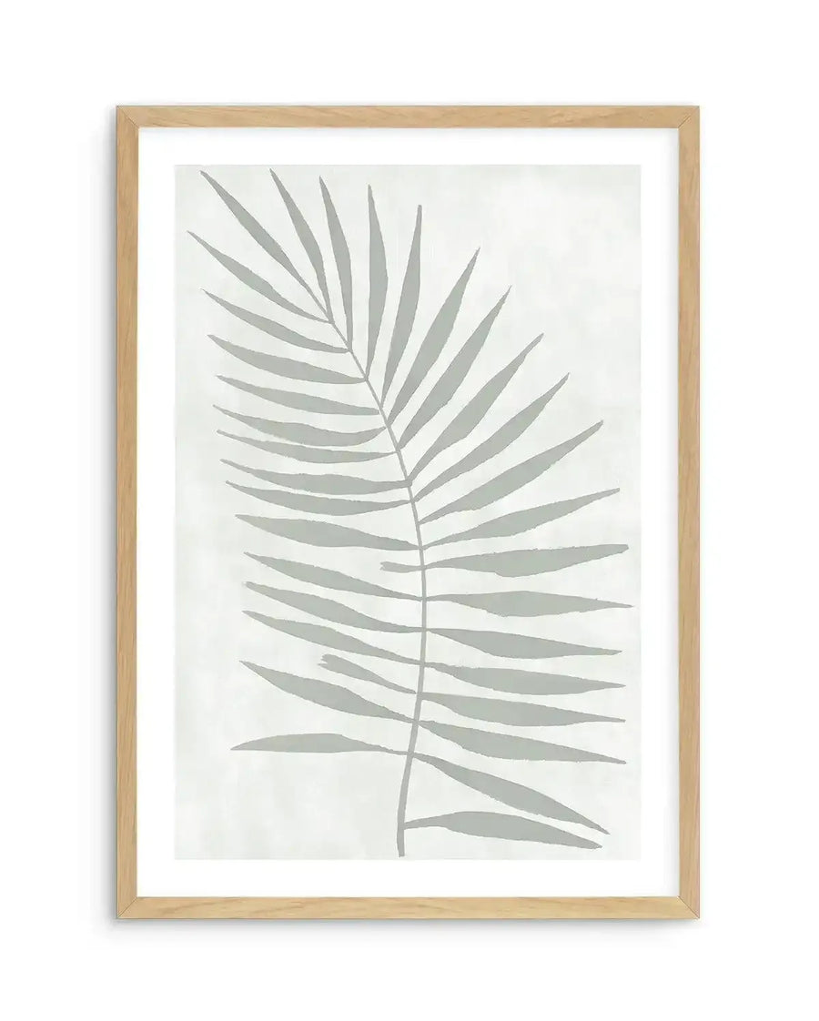 Watercolour art print featuring a single palm frond in a muted sage green against a soft white background, printed on fine art paper and displayed in a natural oak frame with white border.