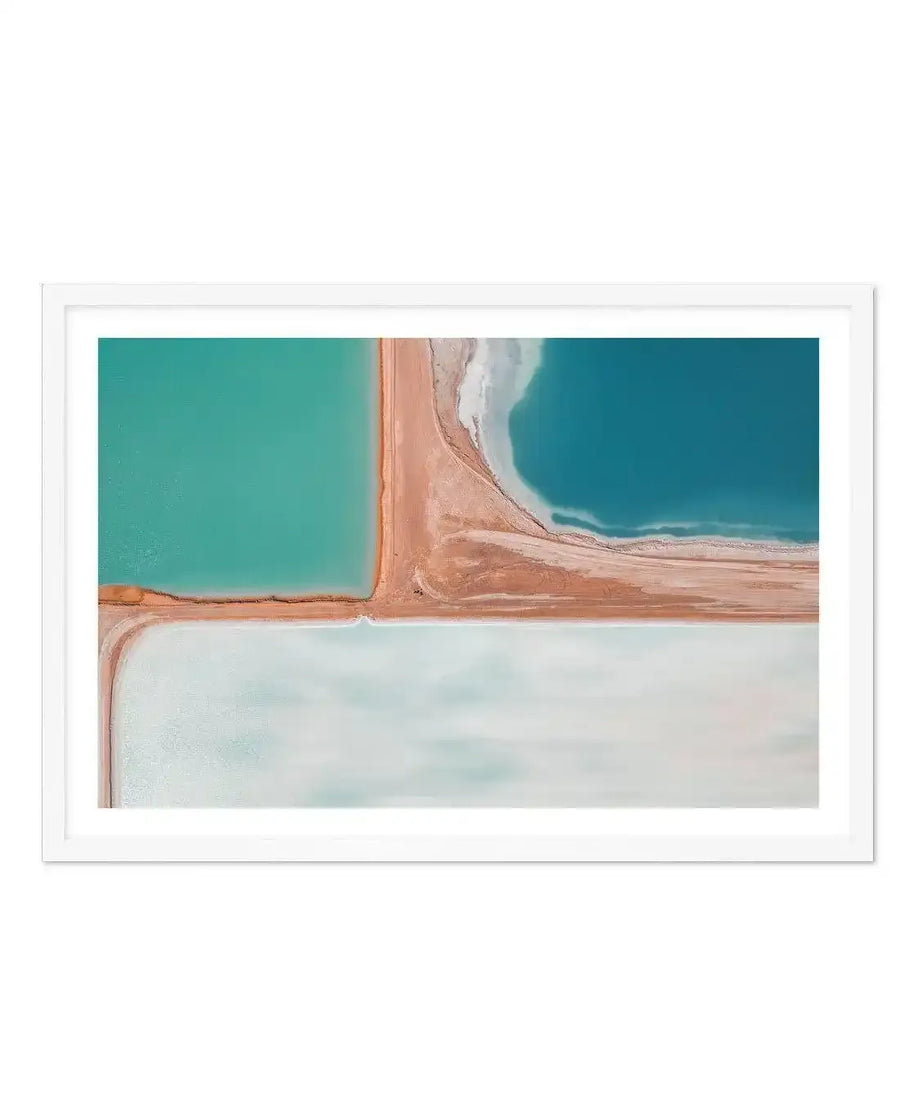 Framed aerial photography print of salt fields with distinct sections of water in varying shades of blue and green, separated by earthy, reddish-brown land formations. The top left section is a vibrant turquoise, the top right is a deeper teal with white, frothy edges, and the bottom section is a pale, milky blue-green, all displayed in a white frame with a white border.