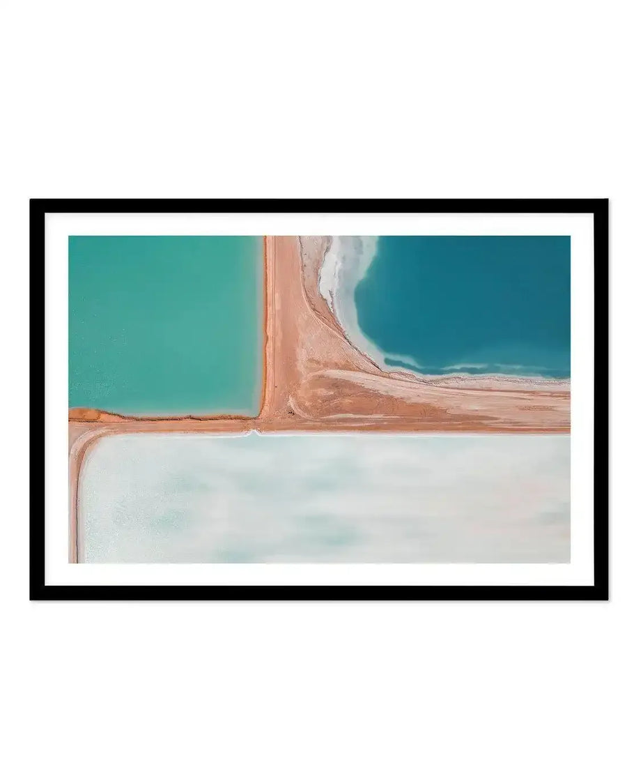 Framed aerial photography art print of salt fields with a black frame and white border. The image is divided into four sections by intersecting sandy paths. The top left section is a vibrant turquoise body of water, the top right is a deeper blue with white foamy edges, and the bottom section is a pale, almost white, body of water with subtle light blue and grey tones.