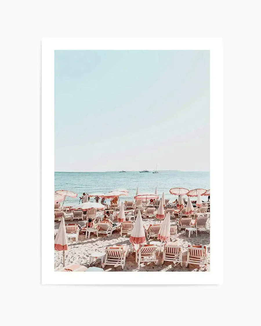 "Photography art print of a vibrant beach scene with a clear blue sky and turquoise ocean, printed on fine art paper. The foreground features rows of white and coral-striped beach chairs and umbrellas on light sand, with people relaxing and swimming in the distance. Several boats are visible on the horizon under a bright, clear sky."