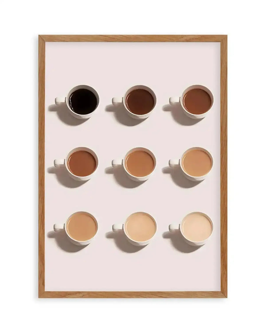 Art print featuring nine white ceramic coffee cups arranged in a 3x3 grid, each containing coffee with varying amounts of milk, creating a gradient from dark black coffee to very light, almost white, milky coffee. The cups are displayed on a pale pink background with subtle shadows, and the print is presented in a natural oak frame with a white border.