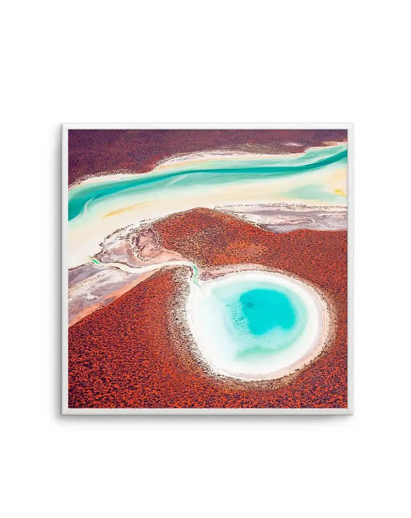 Framed aerial photography art print of Shark Bay, Western Australia, with a white frame and white border. The composition features a vibrant turquoise and white circular lake surrounded by deep reddish-brown land, connected by a narrow channel to a wider, winding river of similar turquoise and white hues, all set against a backdrop of reddish-brown terrain.