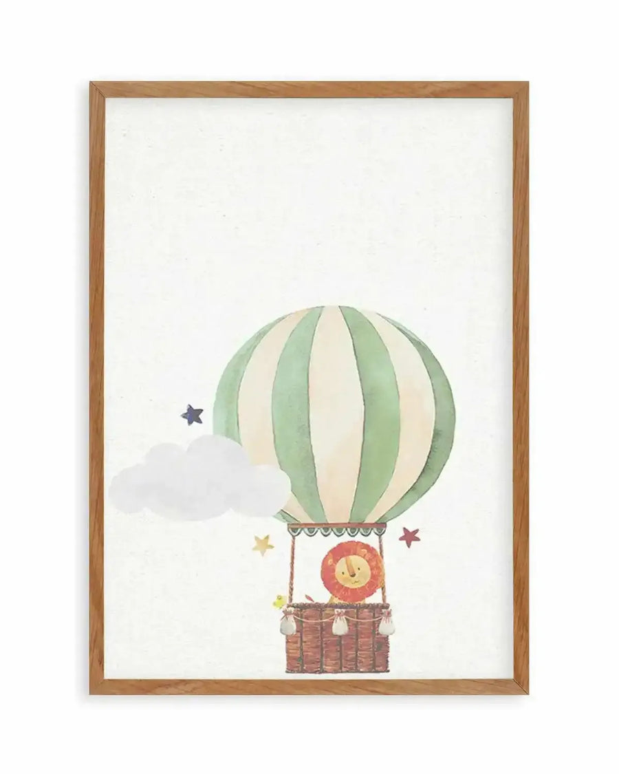 Watercolour art print featuring a hot air balloon with a lion cub in the basket, displayed in a natural oak frame with white border. The hot air balloon is striped in pale green and cream, with a brown woven basket. A smiling lion cub with a red mane peeks out from the basket, accompanied by a small yellow bird. A fluffy white cloud and scattered stars in blue, yellow, and red float around the balloon against a textured white background.