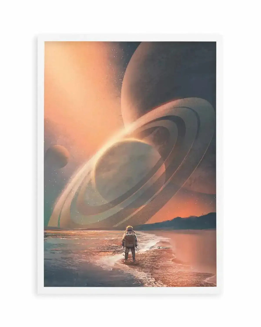 Science fiction art print featuring an astronaut standing on a beach at sunset, looking out at a cosmic landscape with multiple ringed planets and distant stars, displayed in a white frame with white border. The sky is a gradient of warm orange and pink hues, fading into darker blues and purples, with light reflecting off the water and wet sand.