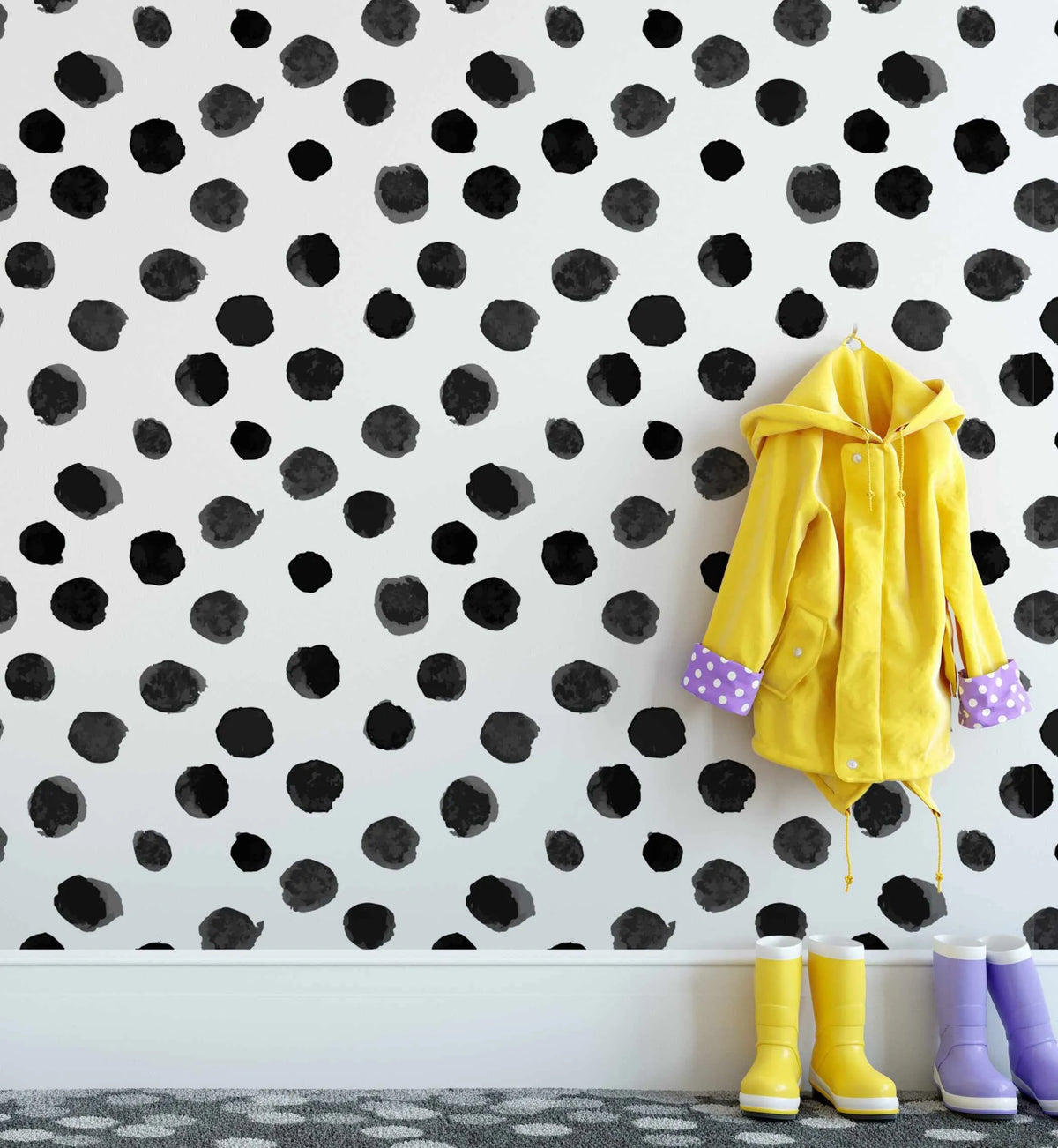 Peel and stick wallpaper featuring a repeating pattern of hand-painted irregular black polka dots with visible brushstroke texture on a clean white background. A bright yellow raincoat with purple polka dot cuffs hangs on a hook, and two pairs of rain boots, one yellow and one purple, sit on a grey patterned rug below.