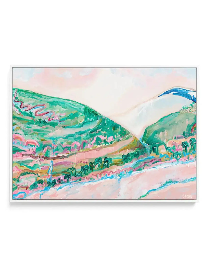 Canvas print featuring an impressionistic landscape painting with rolling hills in various shades of green and pink, a winding red road, and a light pink sky with hints of white clouds. The foreground shows a body of water in light pink and blue, with green trees and pink and green foliage along the banks. The painting has visible brushstroke texture and is displayed in a white frame.