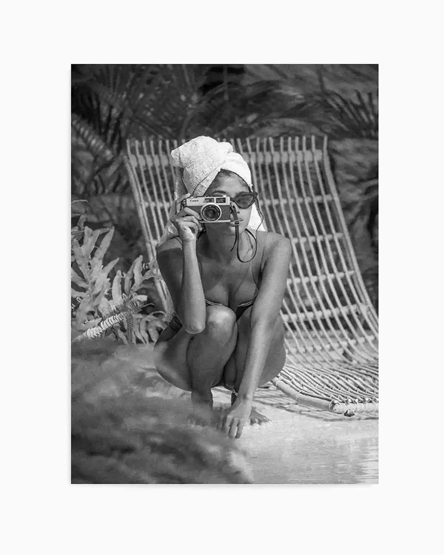 Black and white art print titled "Summer of Love II" by Mario Stefanelli featuring a woman in a crouching pose wearing sunglasses and a white head wrap, holding a vintage camera. She sits against a woven chair or backdrop with tropical ferns visible in the soft-focus background. The photograph-style print captures a candid, leisurely moment with warm, natural lighting and fine detail throughout the composition.