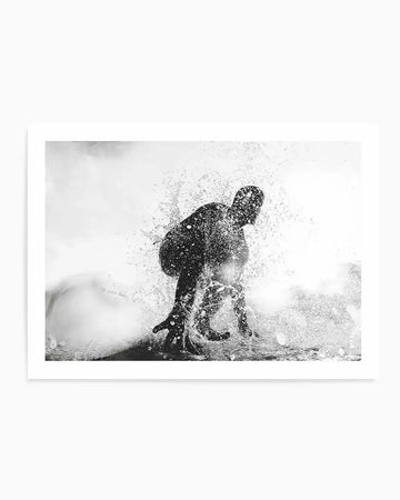 Black and white photography art print of a surfer caught mid-action, surrounded by a dramatic splash of water. The surfer is silhouetted against a bright, almost blown-out background, with water droplets frozen in motion around their body, creating a dynamic and energetic composition.