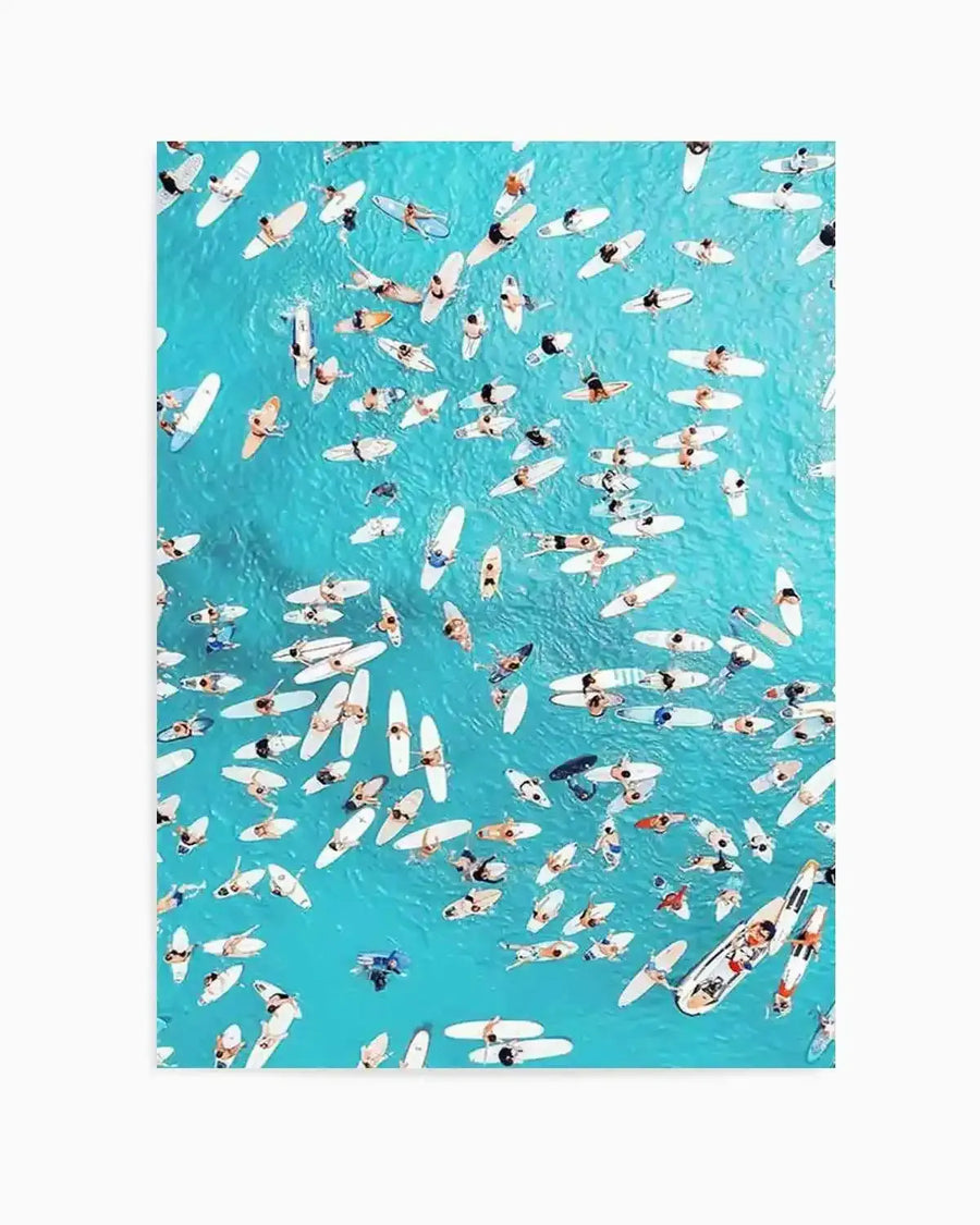 Aerial photograph art print of a vibrant turquoise ocean filled with numerous surfers and their white surfboards, creating a dynamic and crowded scene. The composition captures the surfers from above, some paddling, some lying on their boards, and others sitting upright, all scattered across the bright blue water.