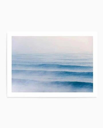 Framed photography art print of a serene ocean scene with gentle, parallel swell lines in varying shades of blue and white, with a soft, misty atmosphere. The composition features multiple horizontal waves rolling towards the viewer, with the foreground showing more detail and white foam, gradually fading into a hazy horizon.