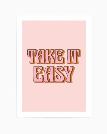 Art print featuring the words "TAKE IT EASY" in two lines, with "TAKE IT" on the top line and "EASY" on the bottom line. The letters are a bubblegum pink with a thick brown outline, set against a soft blush pink background. The typography has a retro, rounded style.