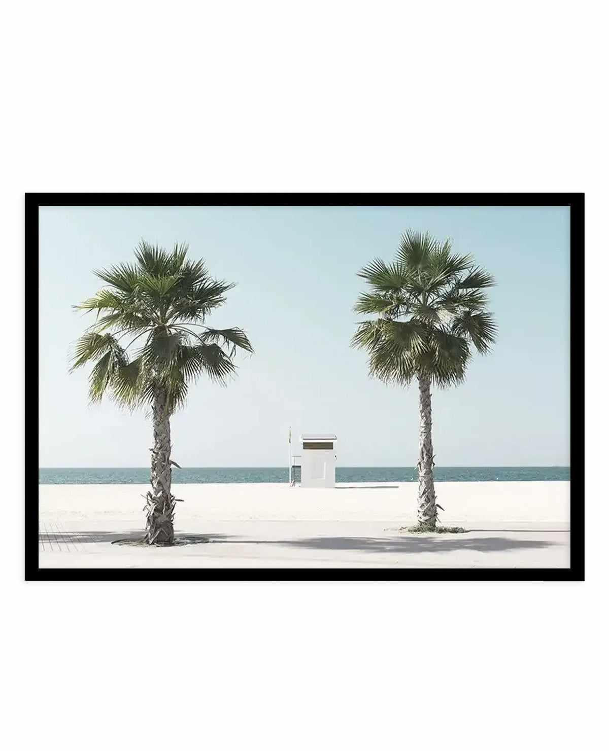 Framed art print featuring a minimalist beach scene with two tall palm trees with fan-like fronds flanking a small white lifeguard station on pale sand. Calm turquoise ocean and clear sky visible in the background. Rendered in a clean, photographic style with muted natural tones of cream, sage green, and soft blue. Black frame with white border.
