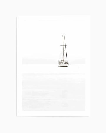 Black and white photography art print featuring a sailboat with two masts anchored in calm, still water under a bright, overcast sky. The composition is minimalist, with the boat positioned slightly to the right of the frame, creating a sense of vast open space. The water and sky blend into a soft, hazy white, with subtle horizontal lines suggesting the horizon and gentle ripples on the water's surface.