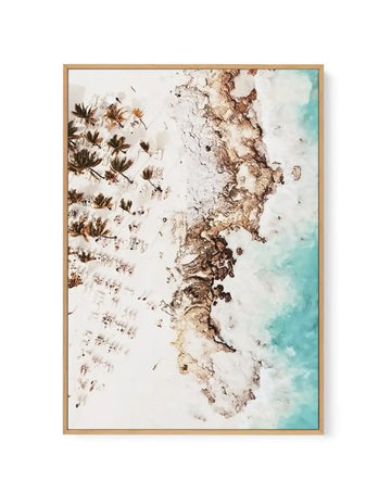 Aerial view canvas print depicting a Tulum, Mexico beach scene framed in natural wood. The composition shows turquoise waters meeting pale sand dotted with palm trees and beach umbrellas arranged in rows. Earth-toned and cream-colored elements dominate the left side with scattered vegetation, while the right side transitions to soft aqua water. The watercolor-style artwork captures a serene coastal landscape with soft, muted tones of brown, tan, white, and turquoise. Natural wood frame with white border.
