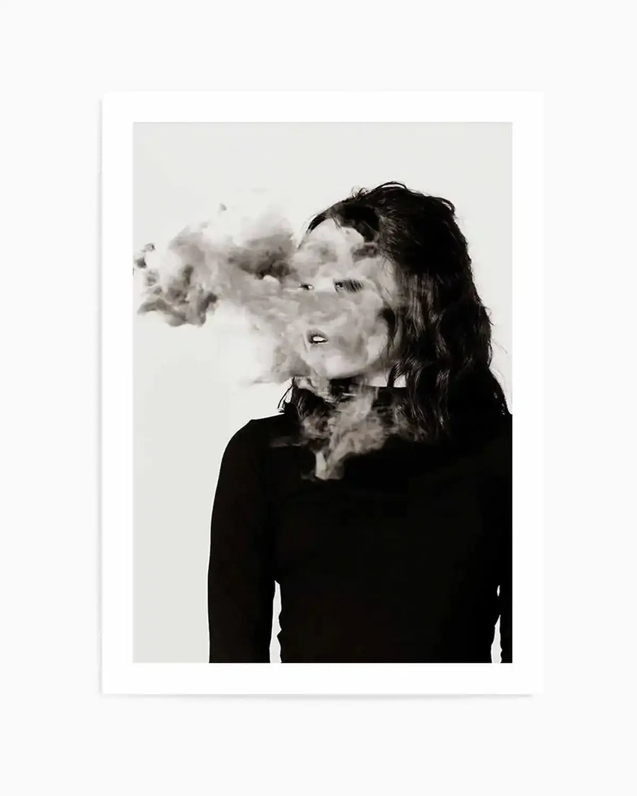 Framed black and white photograph of a woman with dark, wavy hair, shown from the chest up, looking to the right with her mouth slightly open. A large cloud of smoke or vapor obscures part of her face, particularly around her nose and eyes, and billows out to the left. The image has a slightly ethereal or mysterious mood, with a stark white background and a black border around the print.