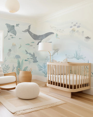 Nursery with pale blue watercolour underwater sea life wallpaper mural, light wood crib and white pouf