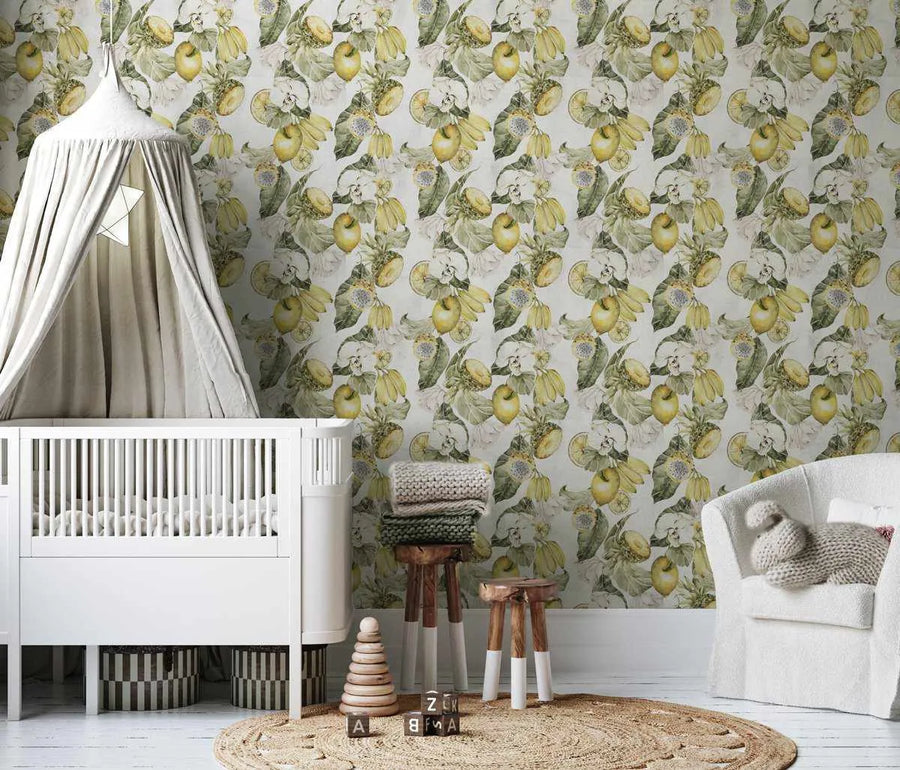 Nursery:
"Peel and stick wallpaper featuring a repeating pattern of hand-painted lemons and green apples with lush green leaves and white blossoms on a soft white background, displayed in a bright and airy nursery. The botanical design has a loose, organic watercolour quality with visible brushstroke texture. A white crib with a light grey canopy stands on the left, and a white armchair is on the right. Wooden stools with knitted blankets and children's toys sit on a round jute rug in the foreground."