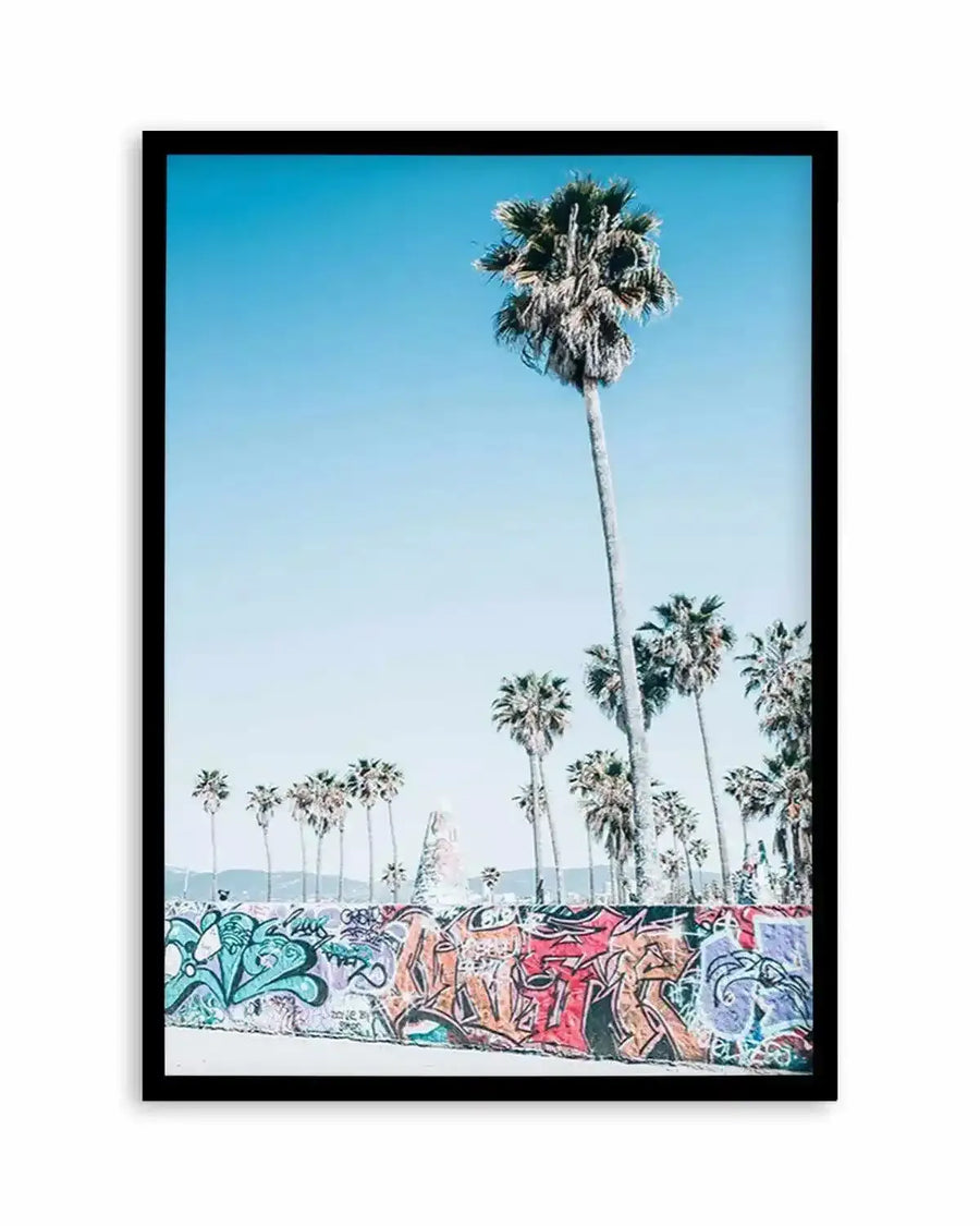 Framed photography art print of a vibrant street scene featuring tall palm trees against a clear blue sky, with a graffiti-covered wall in the foreground. The wall is adorned with colourful street art in shades of teal, orange, red, and purple.
