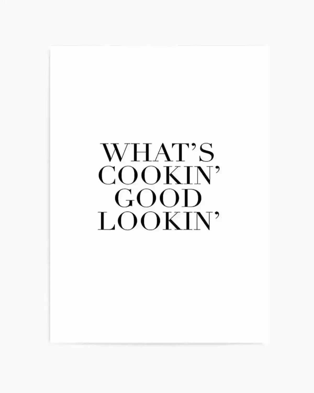 Art print featuring centered black serif typography on a white background reading "WHAT'S COOKIN' GOOD LOOKIN'" in all capitals. The text is evenly spaced across the print in a classic, timeless font. The print has a clean, minimalist design with ample white space surrounding the text. Displayed in a white frame with white border.