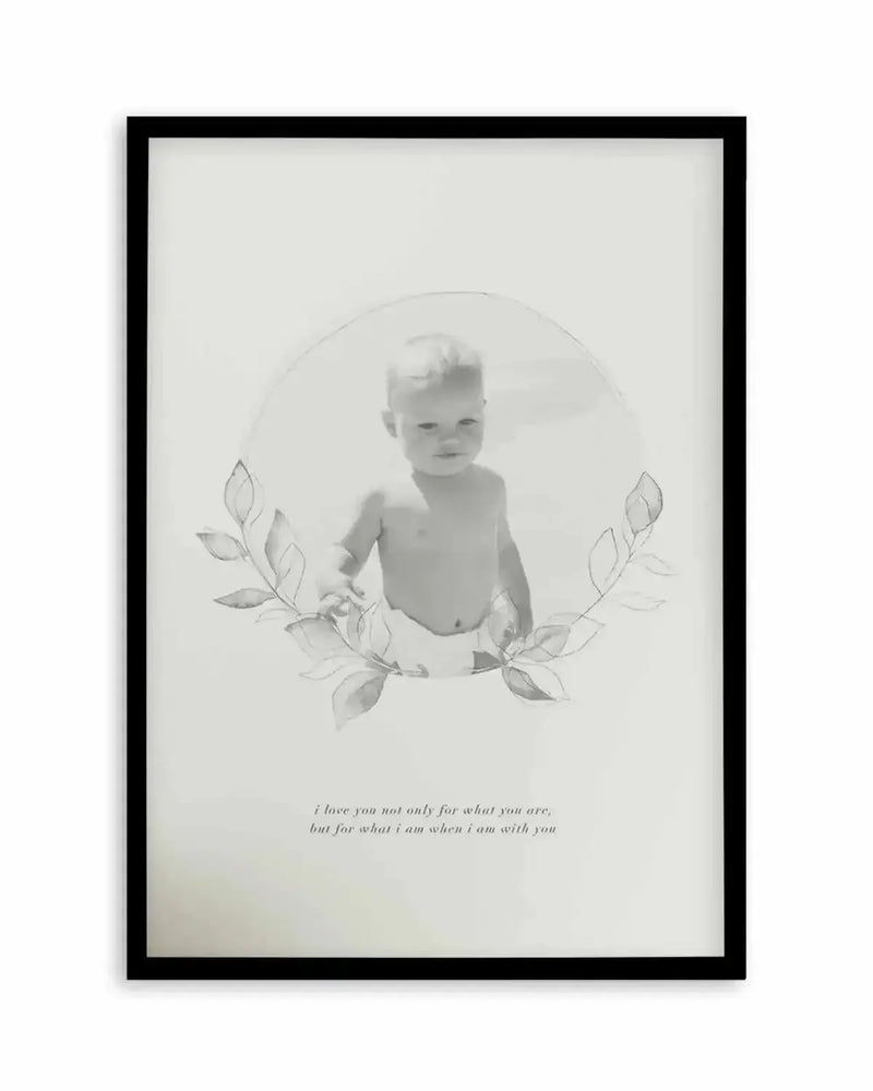 Framed art print with black frame and white border featuring a black and white photograph of a shirtless toddler with light hair, centered within a soft circular vignette. Delicate pencil-drawn leafy botanical branches frame the child on both sides. Below the image, italicized serif text reads "i love you not only for what you are, but for what i am when i am with you." The overall composition has a soft, minimalist aesthetic on a cream-coloured background.
