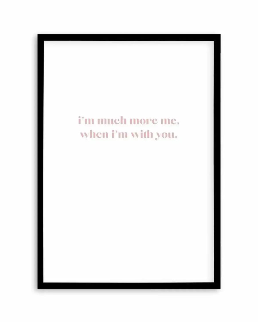 Framed art print with a black wooden frame displaying centered text in soft dusty rose lettering on a white background. The text reads "i'm much more me, when i'm with you." in a modern serif typeface. The minimalist composition conveys an intimate, heartfelt sentiment against the clean white backdrop.