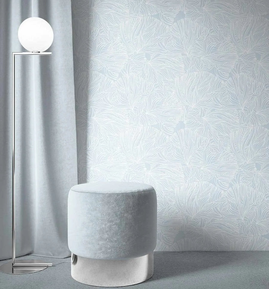 White Coral Wallpaper displayed on a bedroom wall featuring an intricate, organic line-drawn pattern of flowing coral or seaweed-like forms in light gray and white. The repeating botanical design creates a subtle, fluid texture across the wall surface. A minimalist room setting shows the wallpaper beside a cylindrical upholstered ottoman in light gray fabric with a white base, a silver floor lamp with a spherical frosted globe, and sheer white curtains, creating a soft, monochromatic aesthetic.